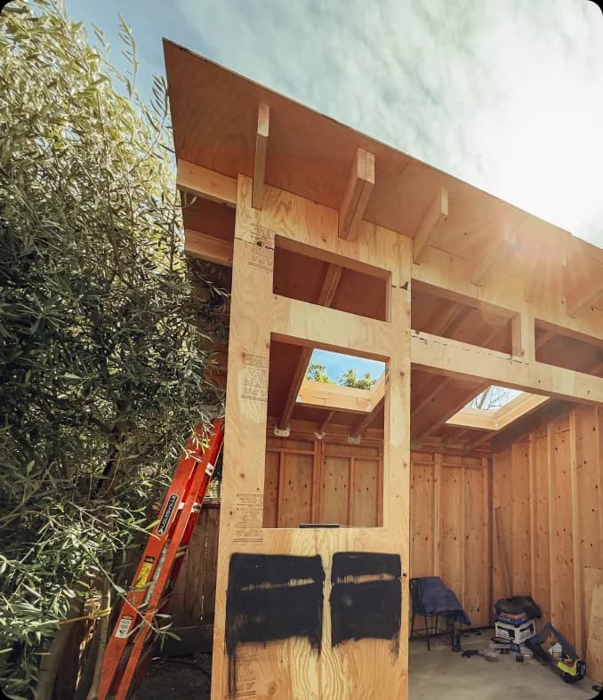 Looking up at a sheathed wall, its window openings cut out and the roof overhang framed above